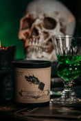 Load image into Gallery viewer, Ghostly Visitor 8oz candle sitting in front of a skull and glass of absinthe
