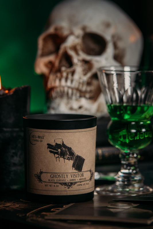 Ghostly Visitor 8oz candle sitting in front of a skull and glass of absinthe