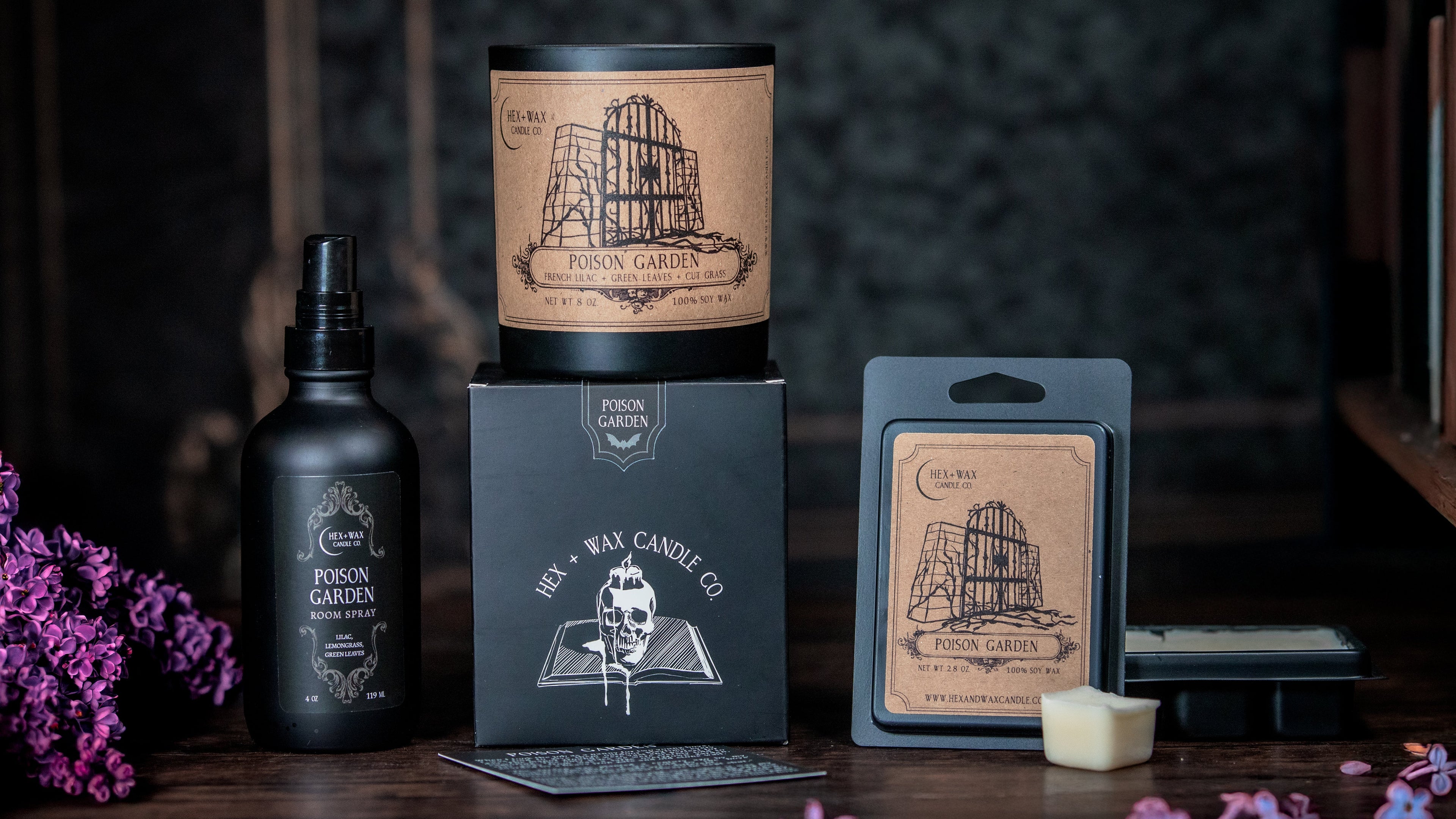 Poison Garden gothic candle with wax melt and room spray by Hex and Wax sitting on a wooden surface with lilac petals scattered around. 